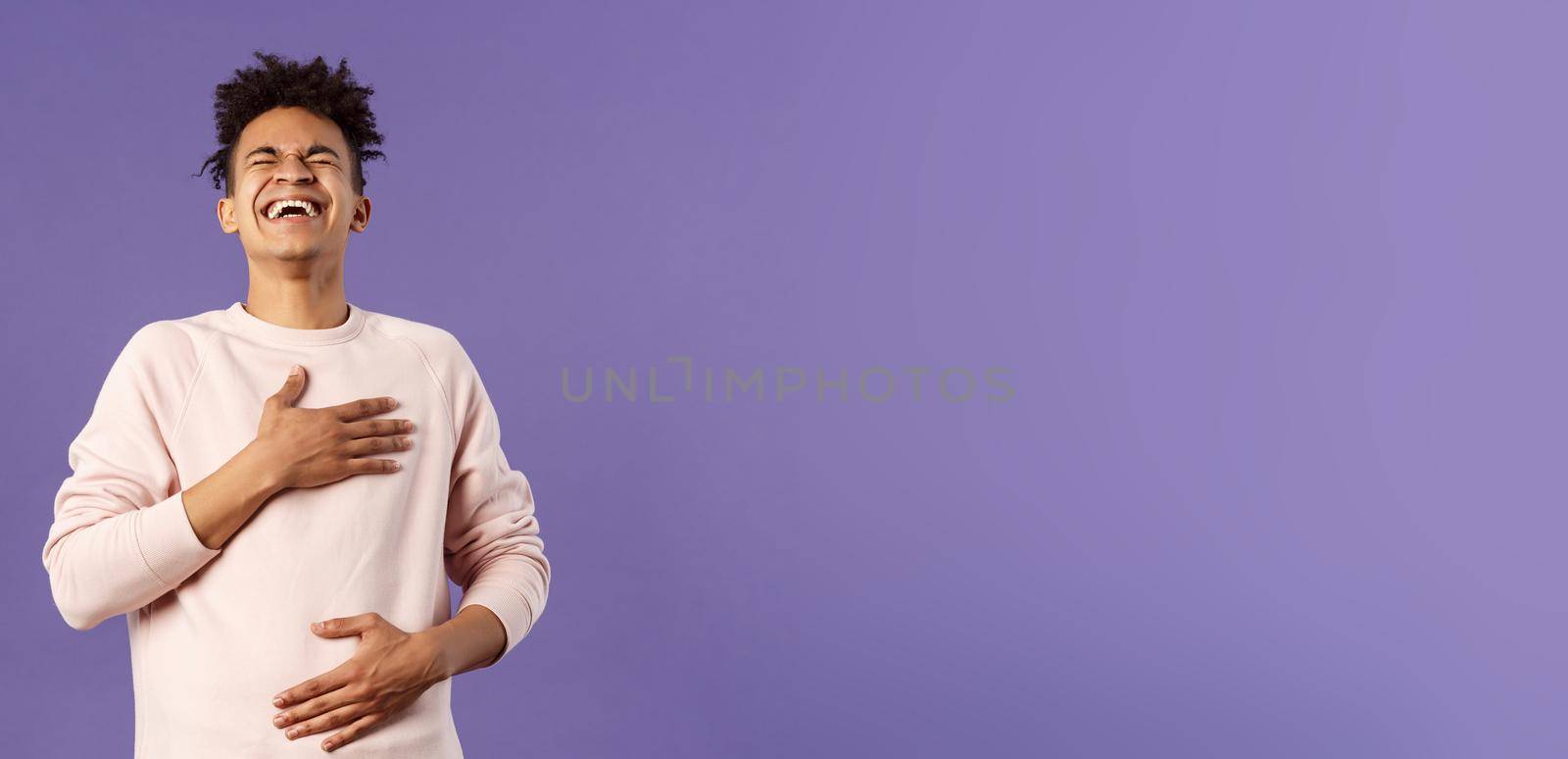 Portrait of cheerful, happy young hipster guy laughing out loud from hilarious joke, watching awesome stand-up performer, chuckle and touchign chest, bending backwards from laugh.