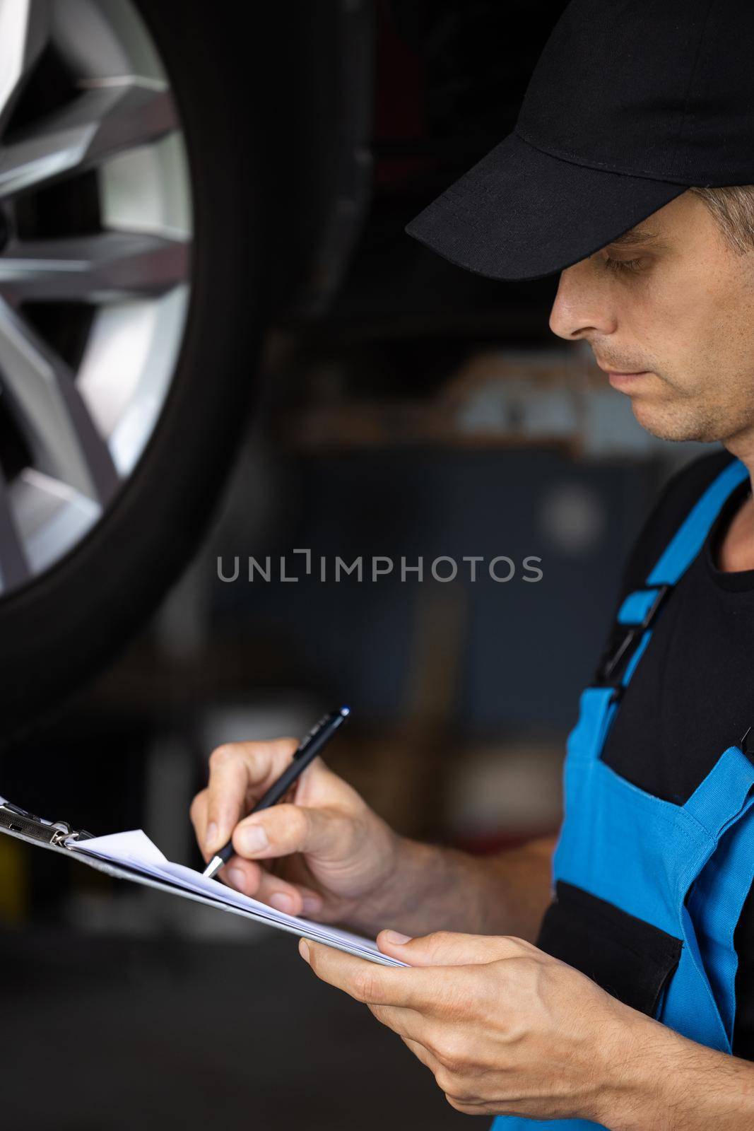 Car service employe inspect car. Mechanic inspects the car undercarriage way and makes a note on his inspection sheet. Automobile service, car mechanic. Modern workshop. by uflypro