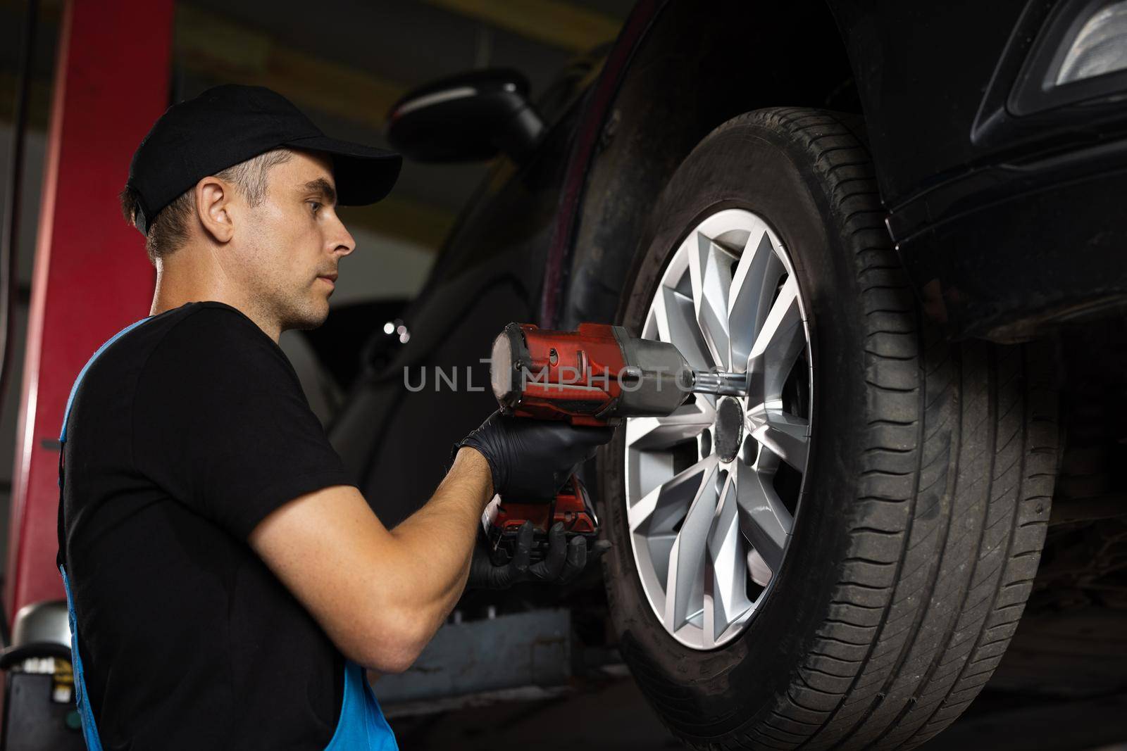 Mechanic is Unscrewing Lug Nuts with Pneumatic Impact Wrench. Repairman Works in a Modern Car Service. Specialists Removes the Wheel in Order to Fix a Component on a Vehicle by uflypro