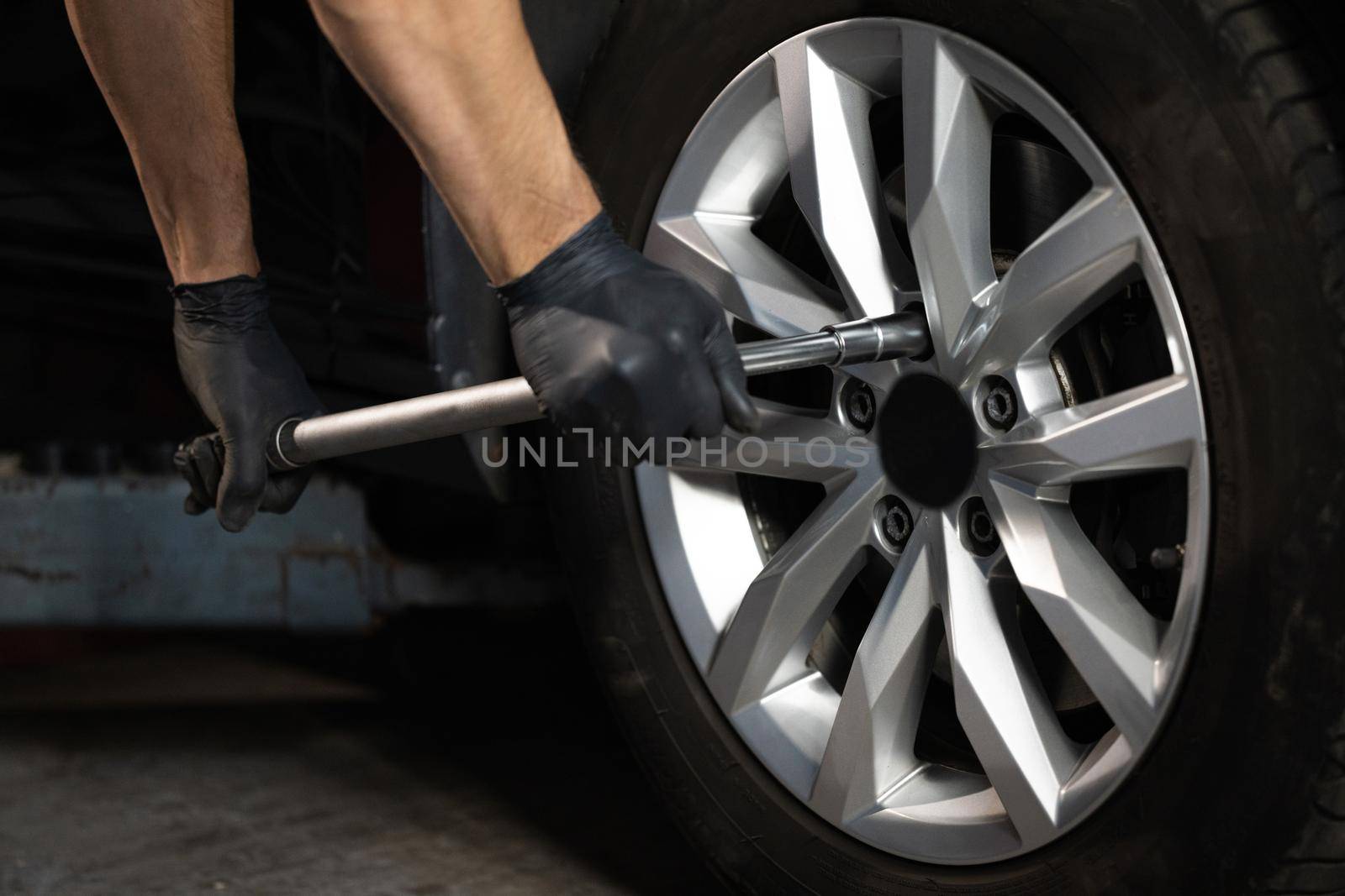 Car mechanic replacing a car wheel tire in garage workshop. Auto service. Repairman mounting wheel tire at service station.