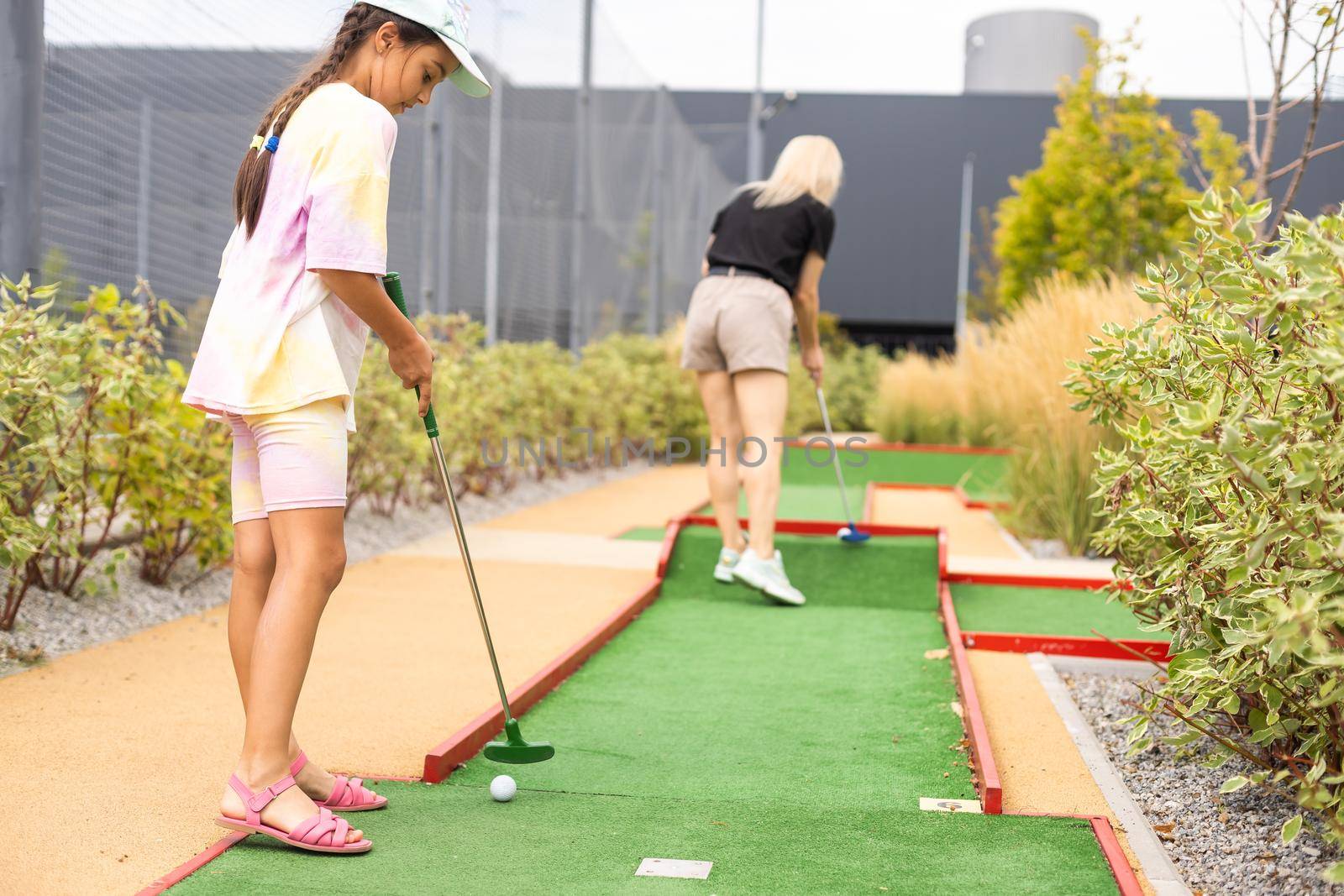 Mother playing with her cute daughter mini golf at outdoor playground