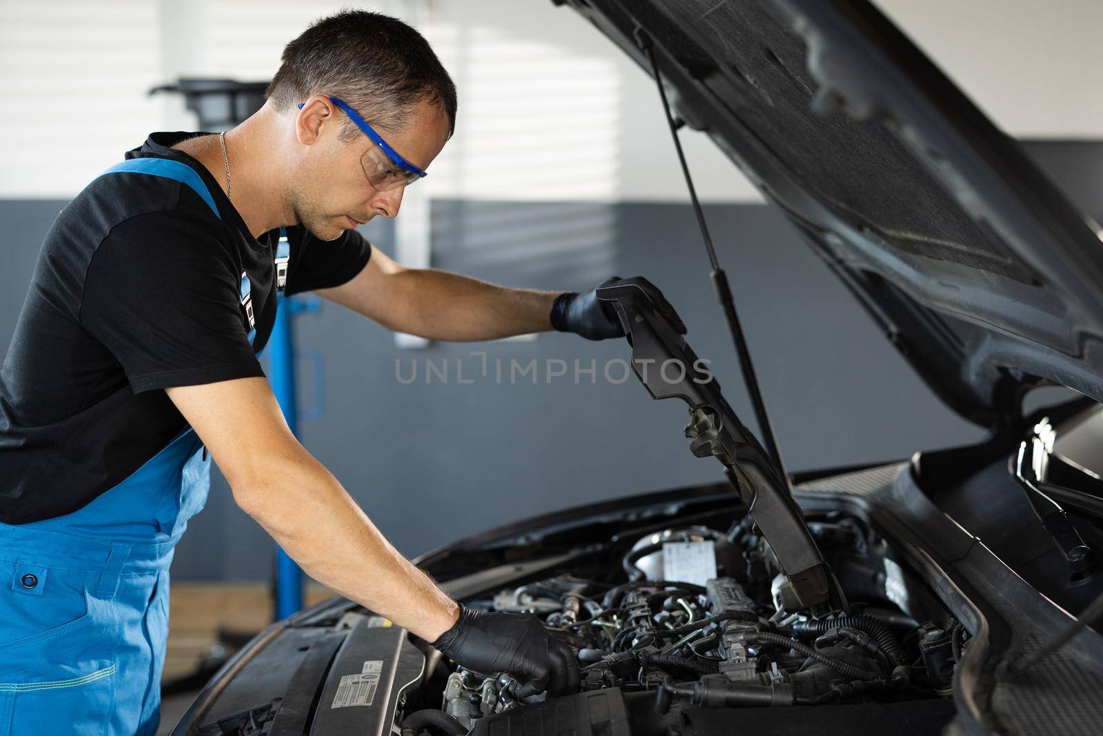 Mechanic man open a car hood and check up the engine. Car mechanic noting repair parts during open car hood engine repair at garage. Overheating of a car engine. Motor with open hood.