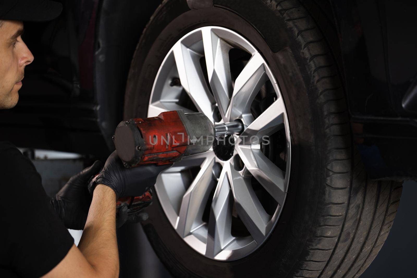 Car mechanic replacing car wheel of lifted automobile at repair service station. Assembly or dismantling of the wheels in the workshop. repair and maintenance of the car in service by uflypro