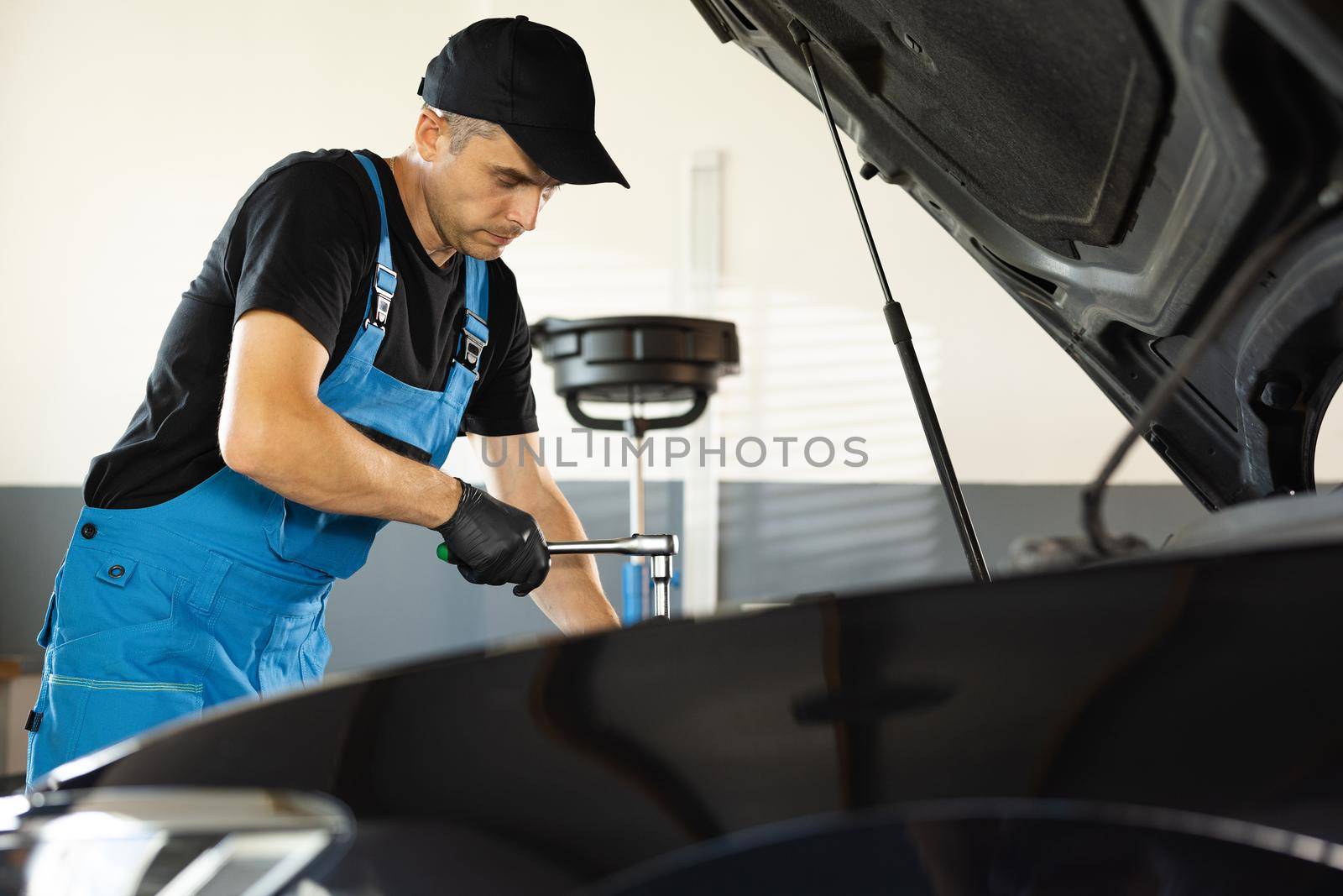 Empowering male mechanic is working in car service. Man is working on an usual car maintenance. He's using ratchet. Car mechanic using wrench to repair the engine, car service. Auto service.