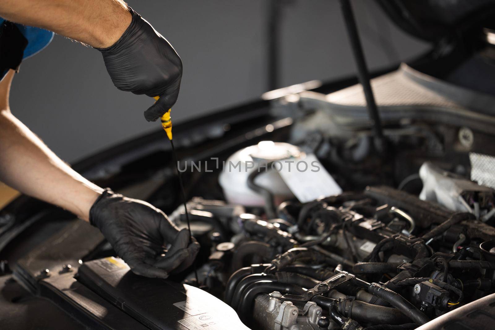 Close-up of automotive mechanic checks the oil level on the car engine dipstick. Car oil quality. Inspection of the engine and checking motor oil level. Man checks the car oil level with dipstick.