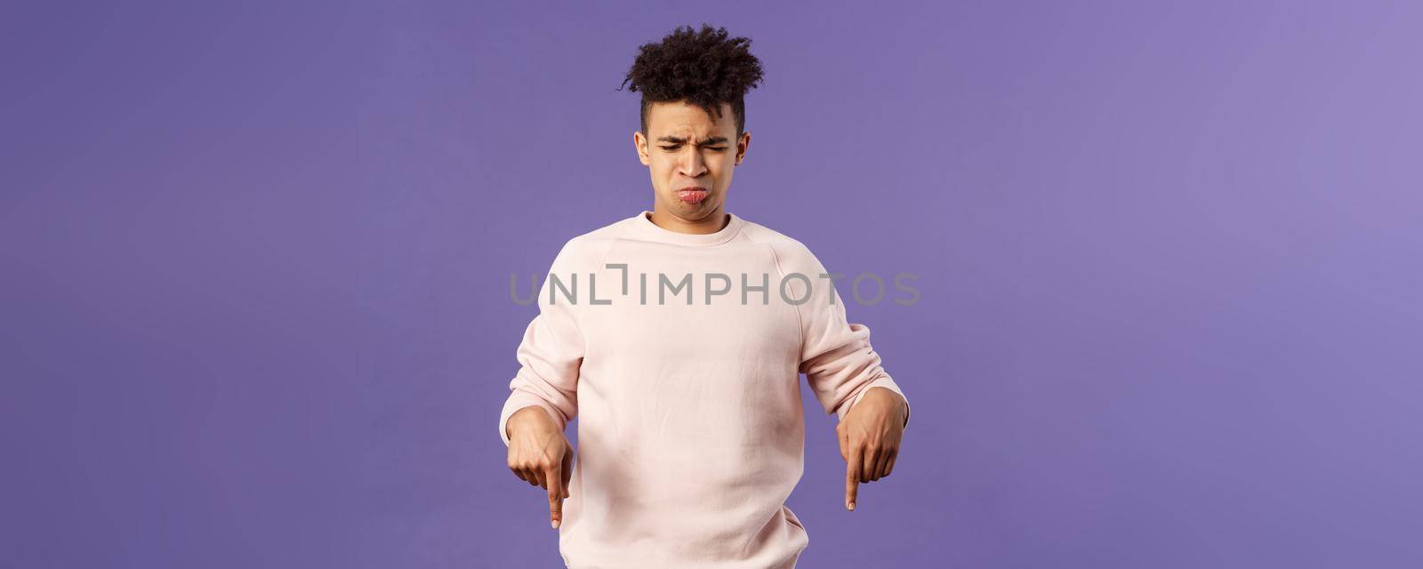 Portrait of gloomy and silly disappointed whining guy, sobbing and crying from envy or jealousy, regret missing chance, looking and pointing down with upset unhappy expression, purple background.