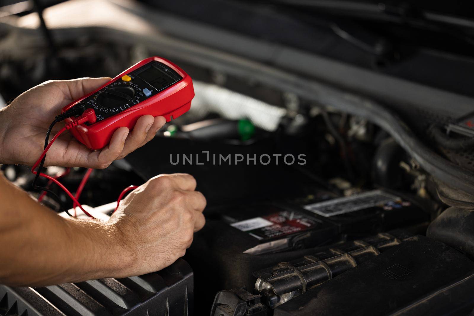 Check battery voltage with electric multimeter. Man using multimeter to measure the voltage of the batteries. Mechanic doing car inspection, he is testing car battery with tester by uflypro