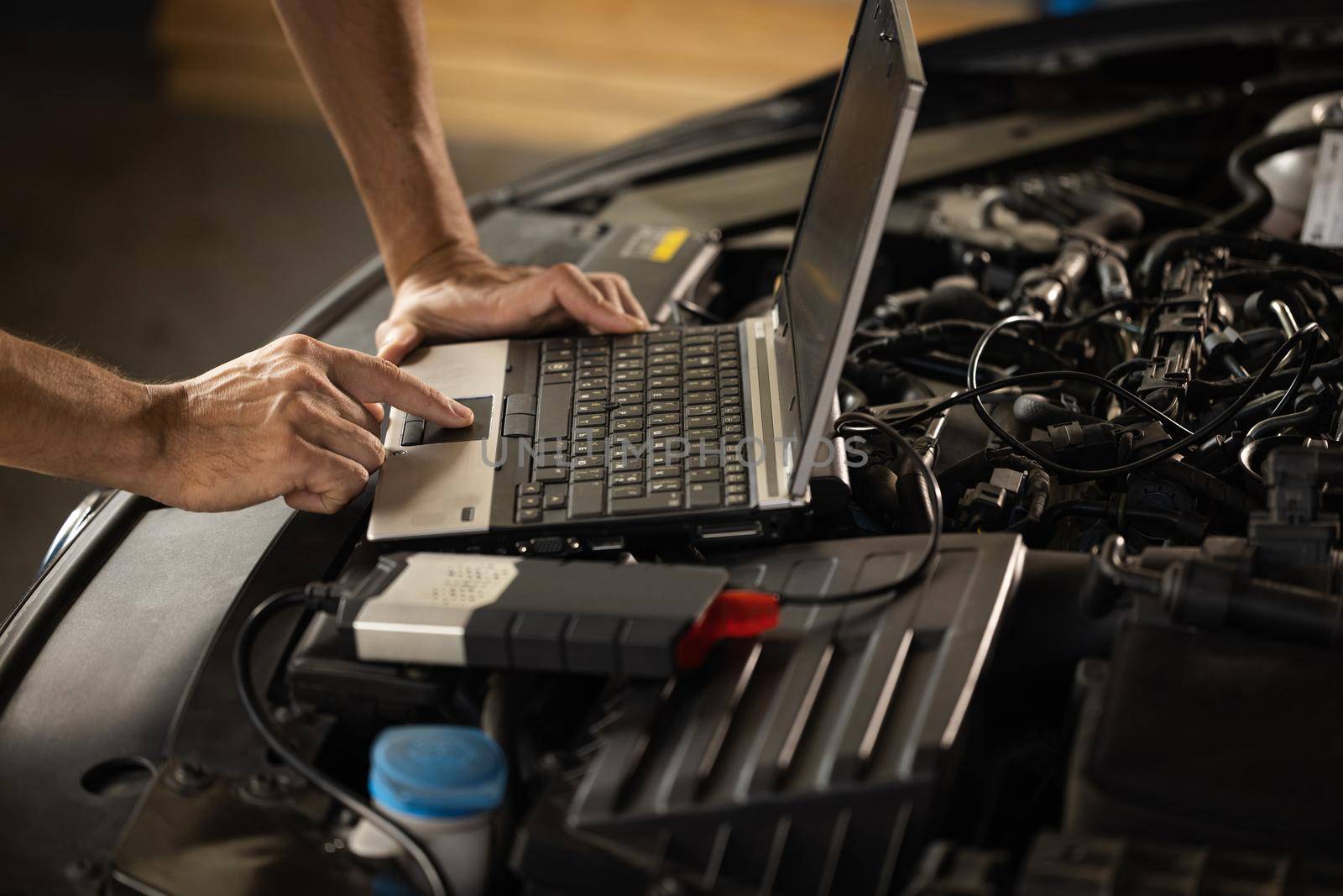 Specialist inspecting the vehicle in order to find broken components and errors in data logs. Automobile service, car mechanic. Auto mechanic uses a laptop while conducting diagnostics test by uflypro