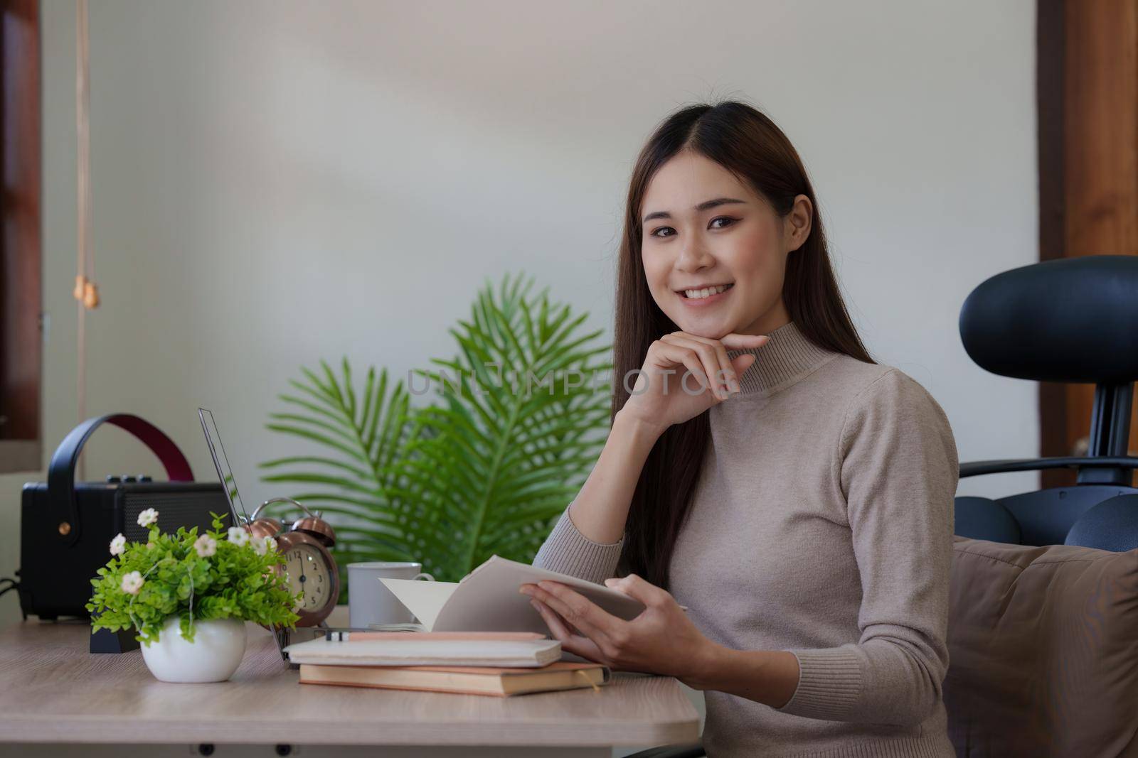 Beautiful Asian Woman reading a book at her desk at home.