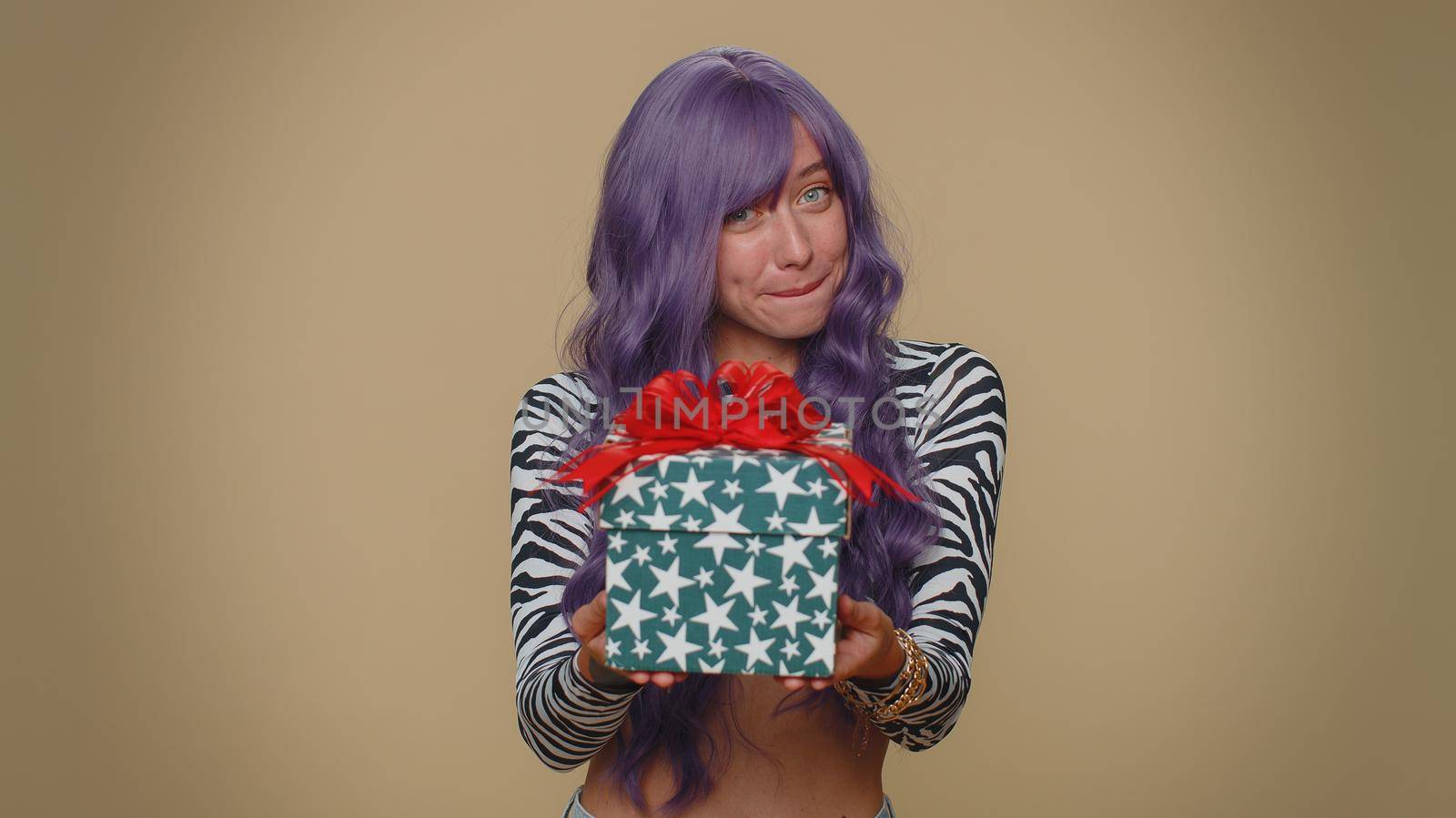 Positive smiling lovely pretty young woman presenting birthday gift box stretches out hands, offer wrapped present career bonus, celebrating party. Adult stylish girl on beige studio background indoor