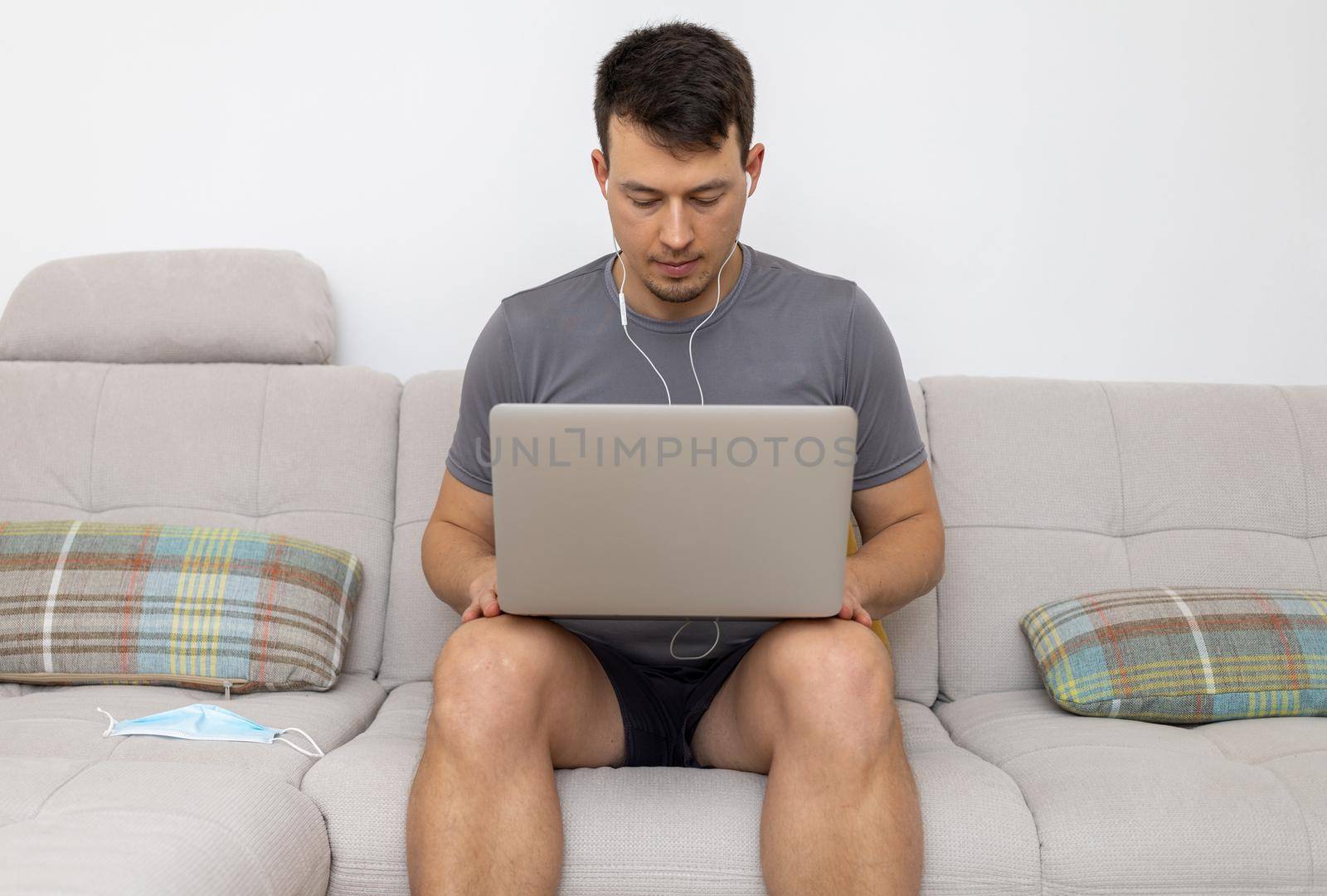 young man in headphones and with laptop sitting on sofa by Chechotkin