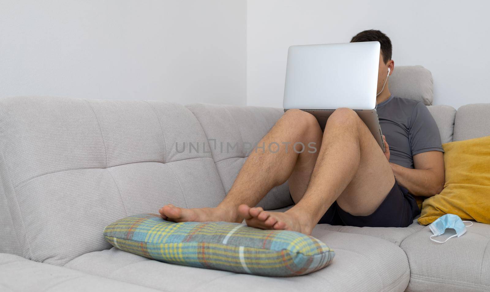 young man with laptop sitting on sofa with legs by Chechotkin