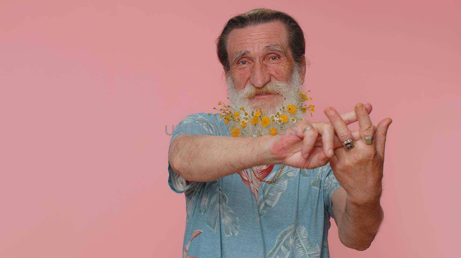 Cheerful senior man with flowers in beard showing hashtag symbol with hands, likes tagged message, popular viral content, sign to follow internet online trends. Elderly grandfather on pink studio wall