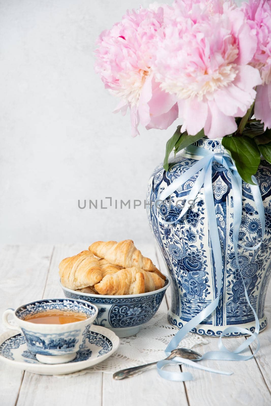 spring still life with croissants and a bouquet of pink luxurious peonies in an ancient Chinese vase with blue ornament, an antique tea cup, early breakfast or brunch, High quality photo