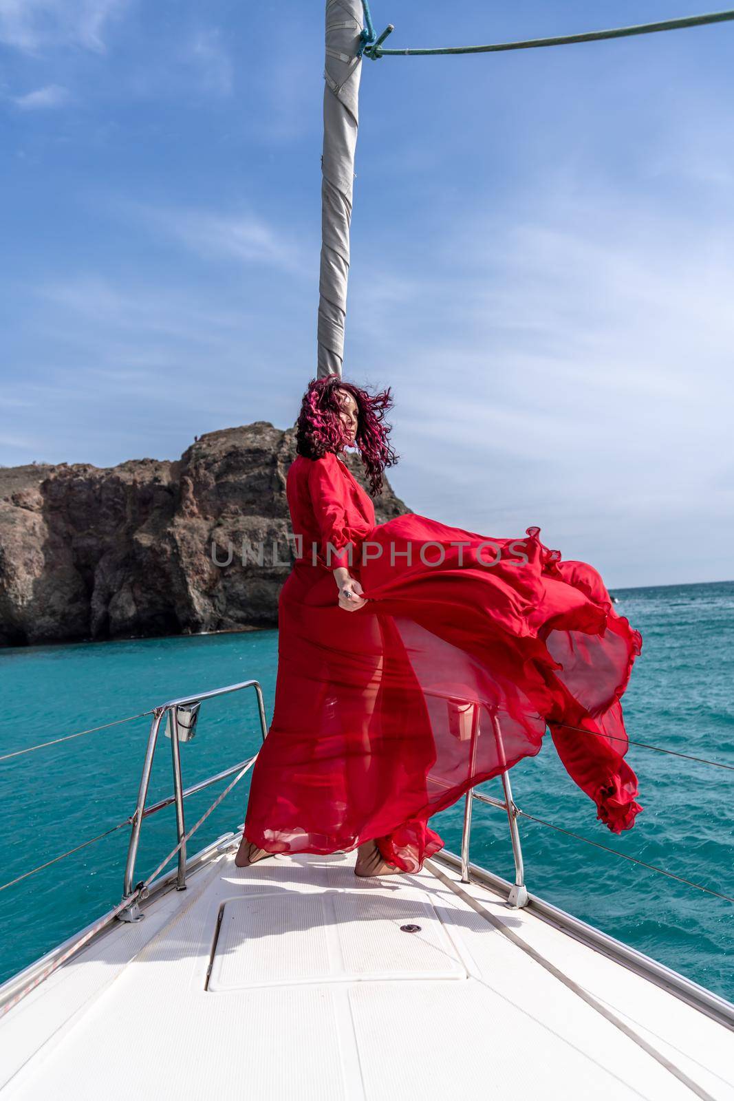 Attractive middle-aged woman in a red dress on a yacht on a summer day. Luxury summer adventure, outdoor activities