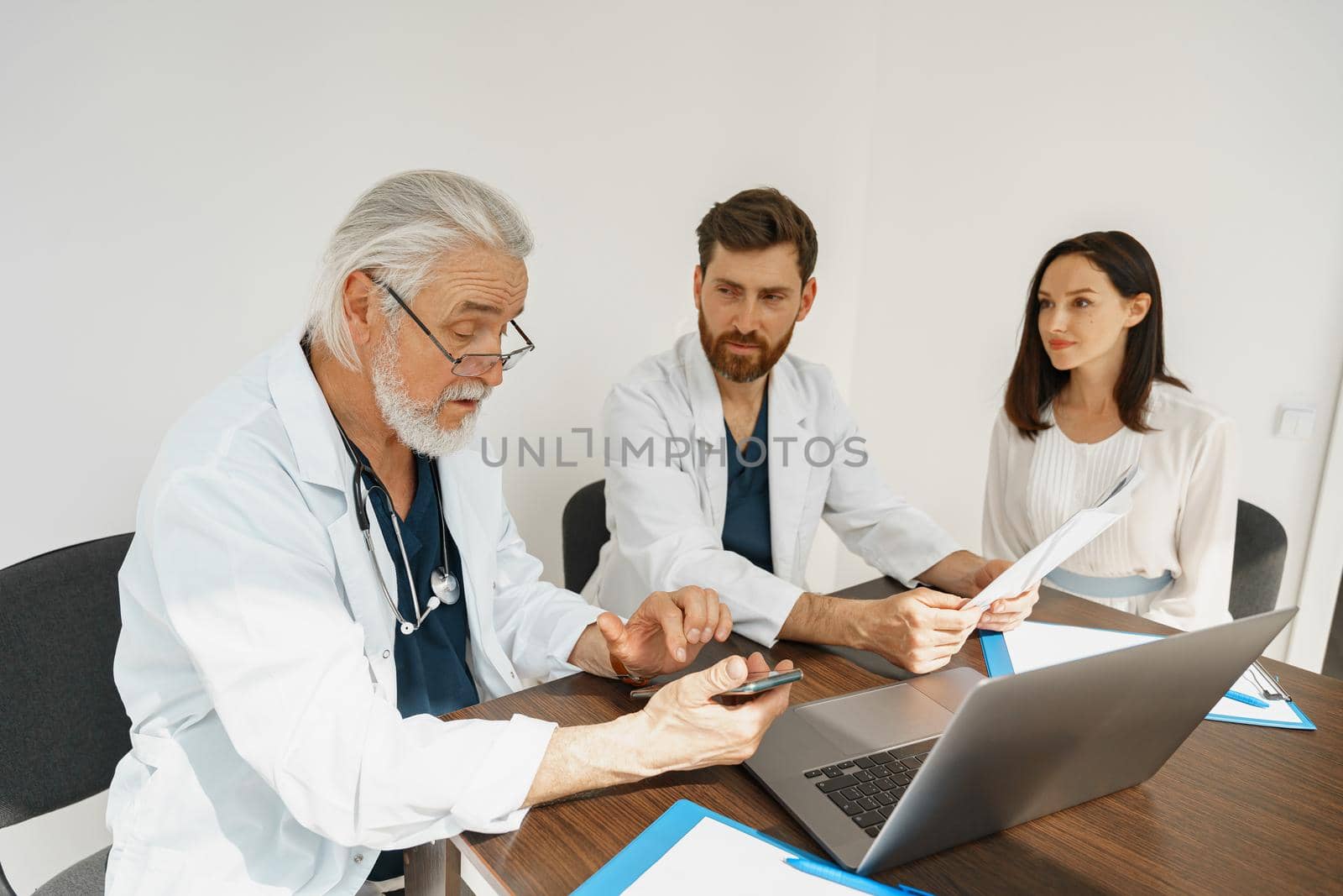 Two doctors in white uniform consult female patient at meeting in private clinic. High quality photo