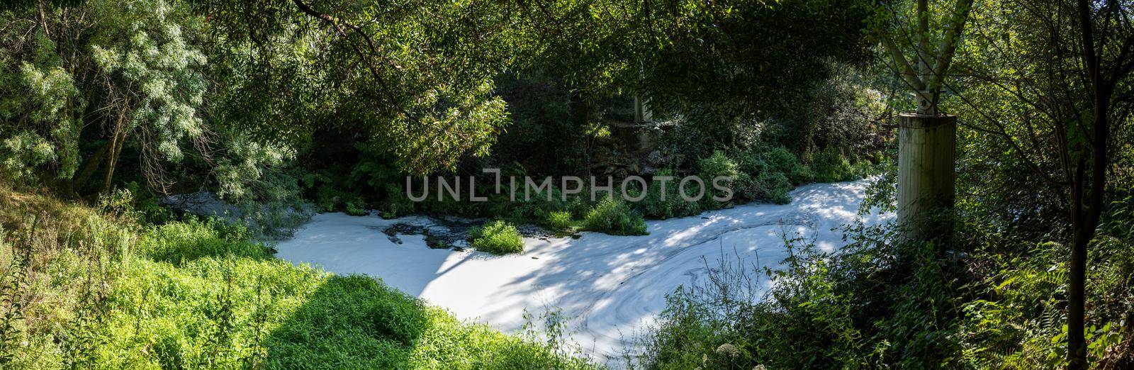 View from under the bridge of white foam pollutants swirling across the water surface floating on river Caima, Palmaz - Oliveira de Azemeis - Portugal.