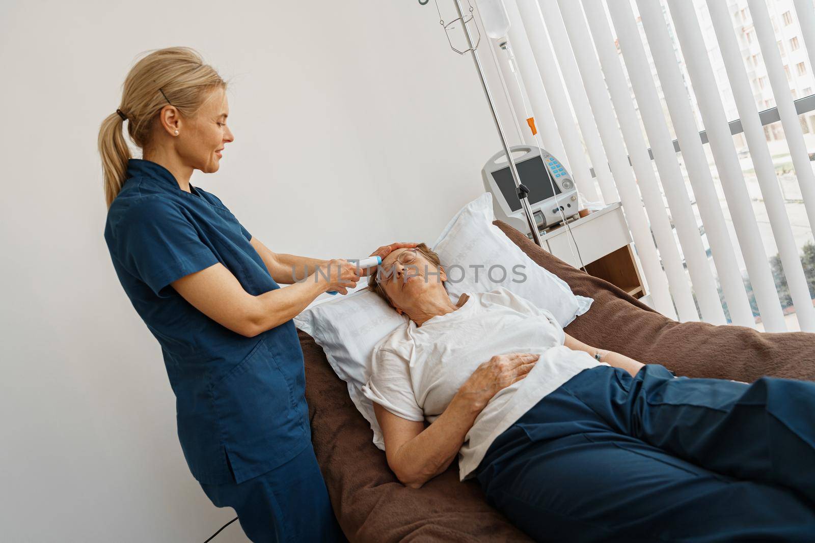 Doctor measures patient's temperature with non-contact thermometer during treatment in hospital ward