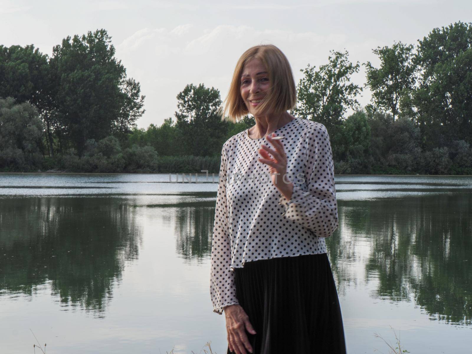 female pensioner having fun and smoking a cigarette in a park - aging free and wellness concept