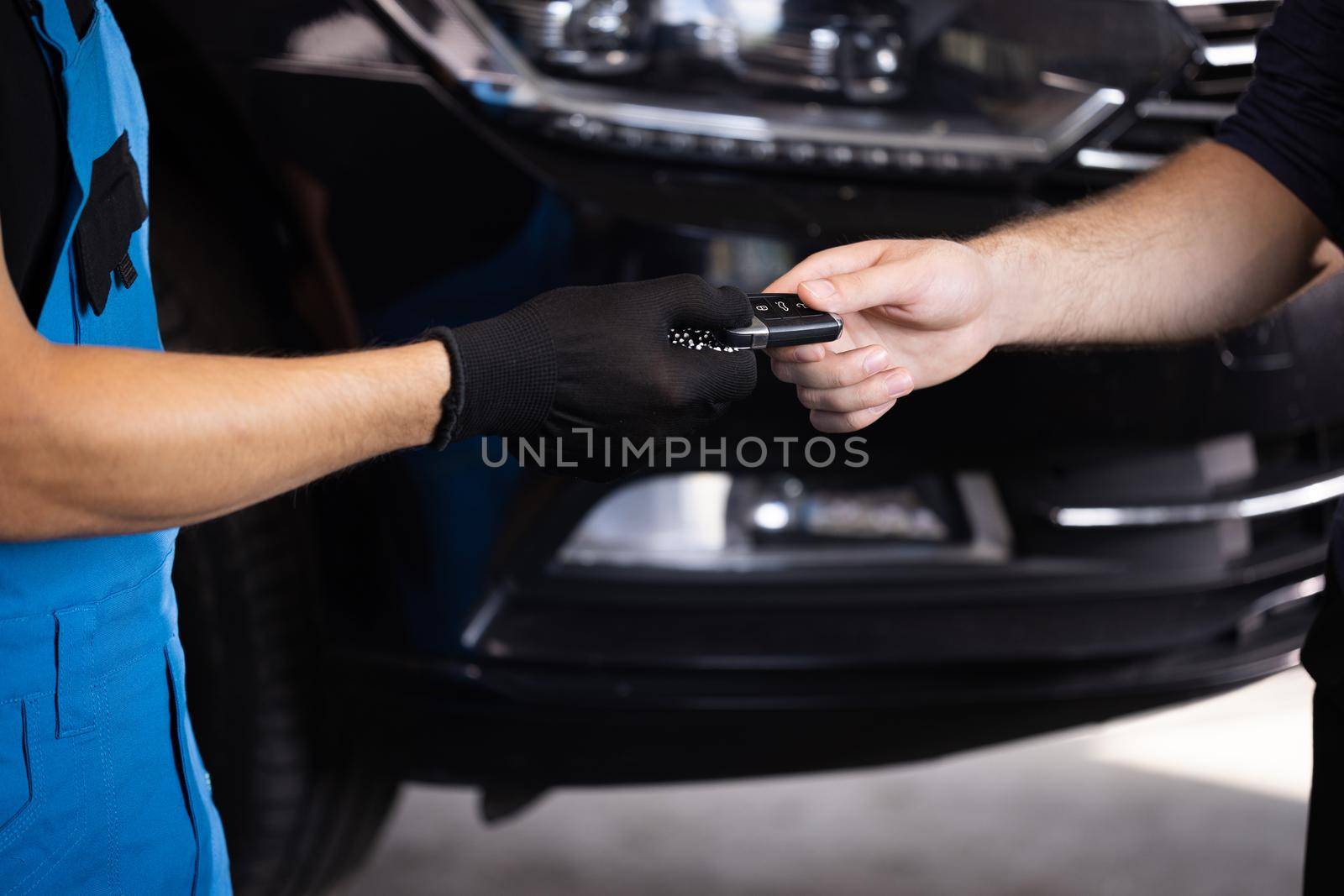 Close up shot of hands of mechanic giving car key to male client after servicing in auto repair shop. Vehicle breaks down. Car repair.
