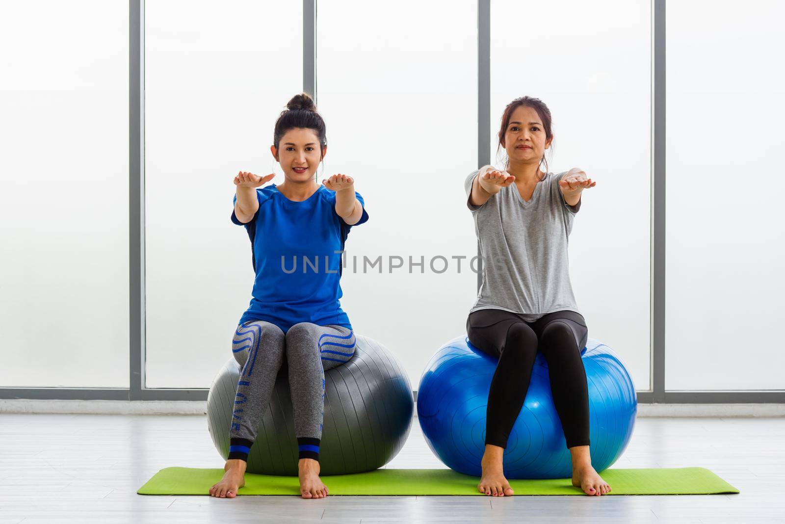 Two Asian adult and young woman in sportswear doing aerobics yoga exercise with sitting on fitness ball indoor yoga studio, fit sport healthy workout lifestyle exercise