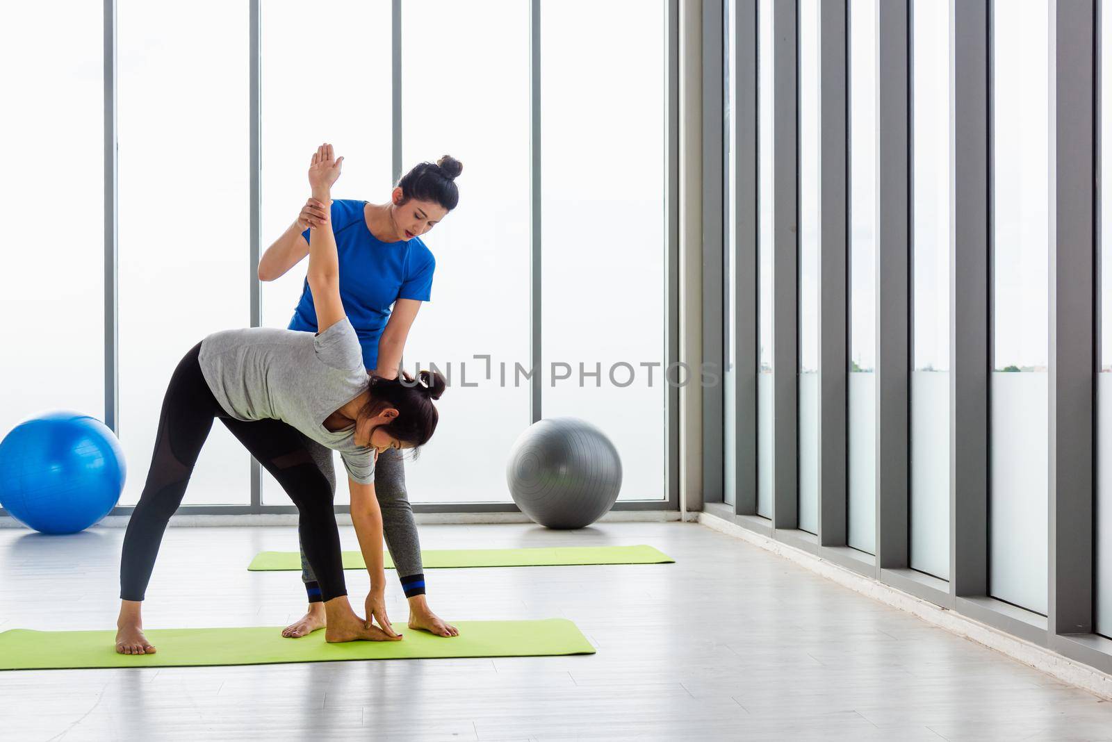 Asian young woman teacher teach adult student doing yoga stretching position in studio. Two woman teaching yoga and fun together, female sport fit workout concept
