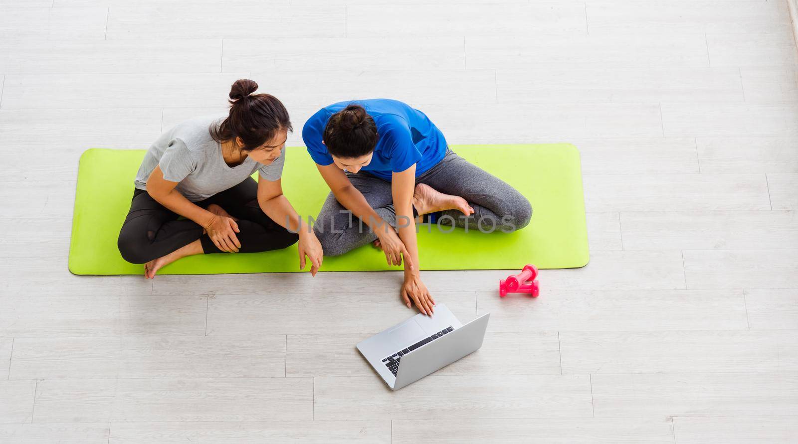 Overhead two Asian lifestyle adult and young woman in sportswear sitting floor on mat with dumbbells look laptop computer for training videos online in yoga studio, fit sport healthy workout exercise