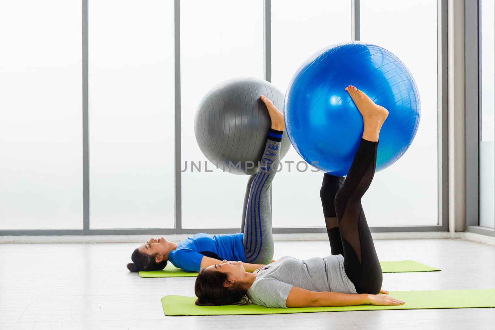 adult and young woman in sportswear doing aerobics yoga exercise abdominal with fitness ball by Sorapop