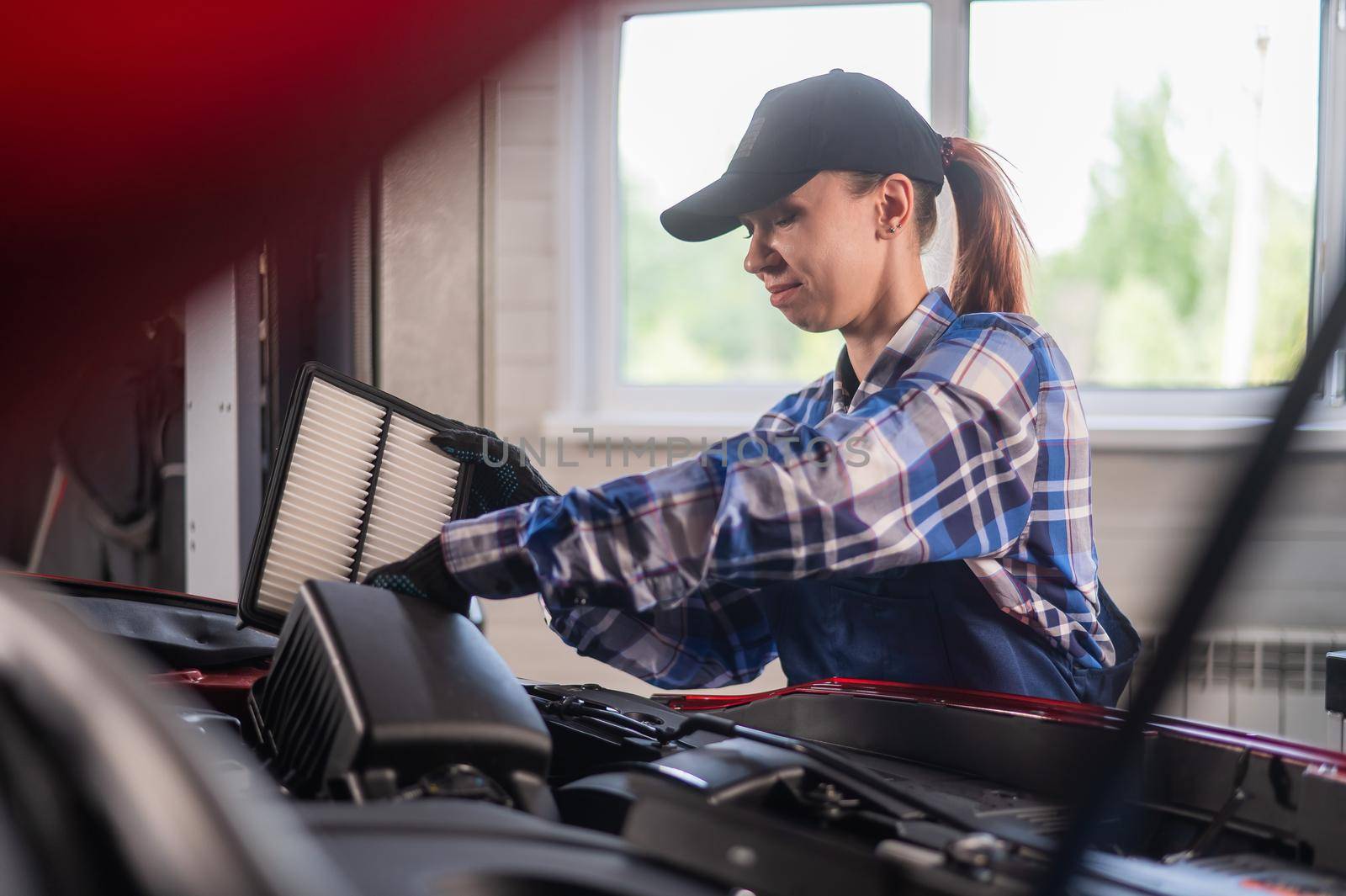 Caucasian female auto mechanic changes the engine air filter in the car