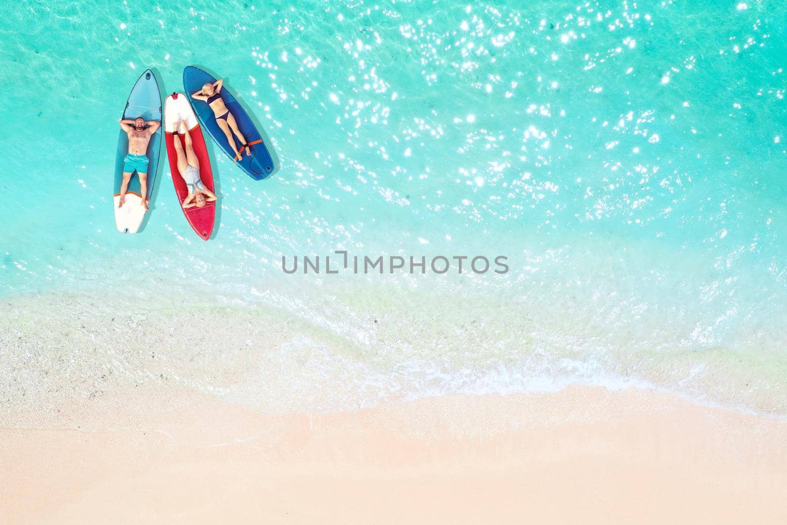 The family is resting lying on Sup boards in the turquoise sea. Three people ride sup boards in the ocean near the beach.