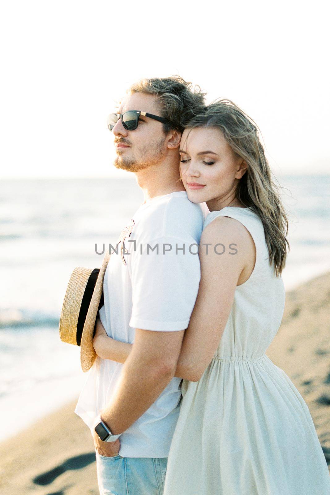 Woman hugging man from behind while standing on the beach by the sea. High quality photo