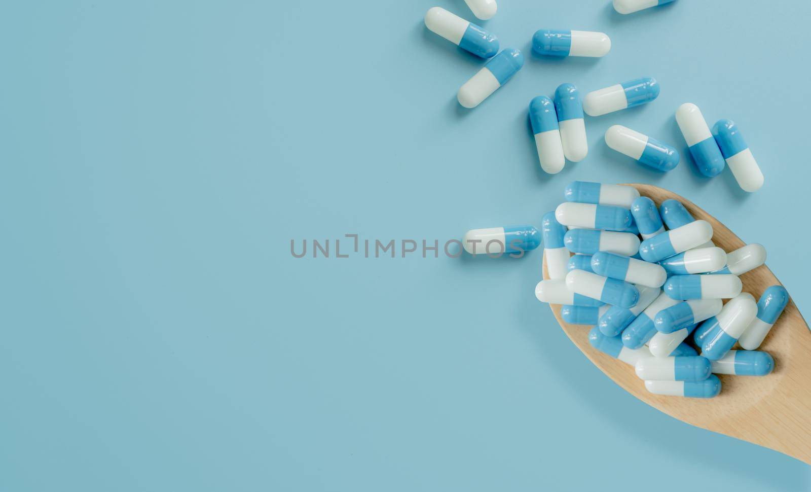 Top view of blue-white antibiotic capsule pills on wooden spoon and blue background. Antibiotic drug resistance. Prescription drug. Medical care. Pharmaceutical care. Antimicrobial drug overuse.