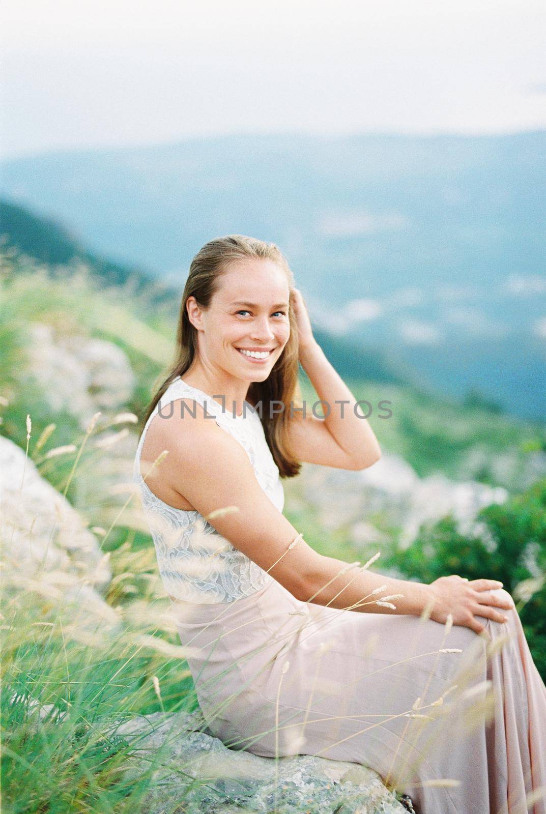 Smiling girl straightens her hair with her hand while sitting on a stone in the mountains. High quality photo