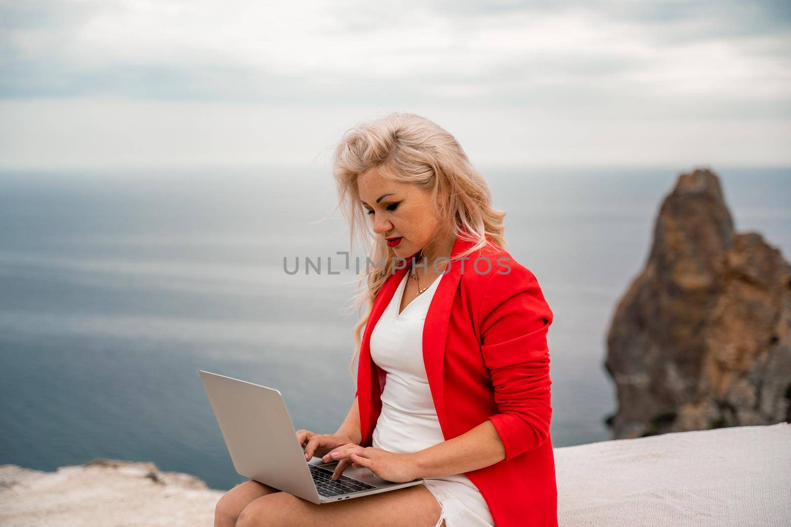 A woman is typing on a laptop keyboard on a terrace with a beautiful sea view. Freelancing, digital nomad, travel and vacation concept