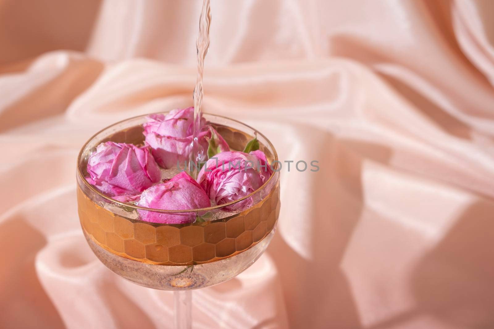 Champagne with flowers in glass on folded fabric background. Creative holiday concept.