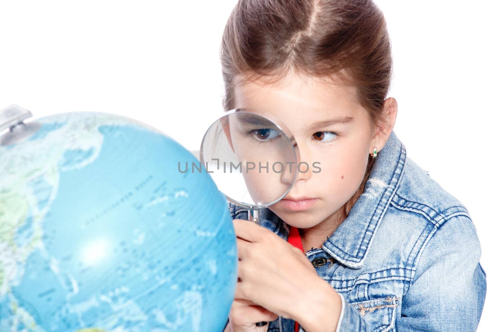 Curious little girl looking through magnifying glass on globe by Taut