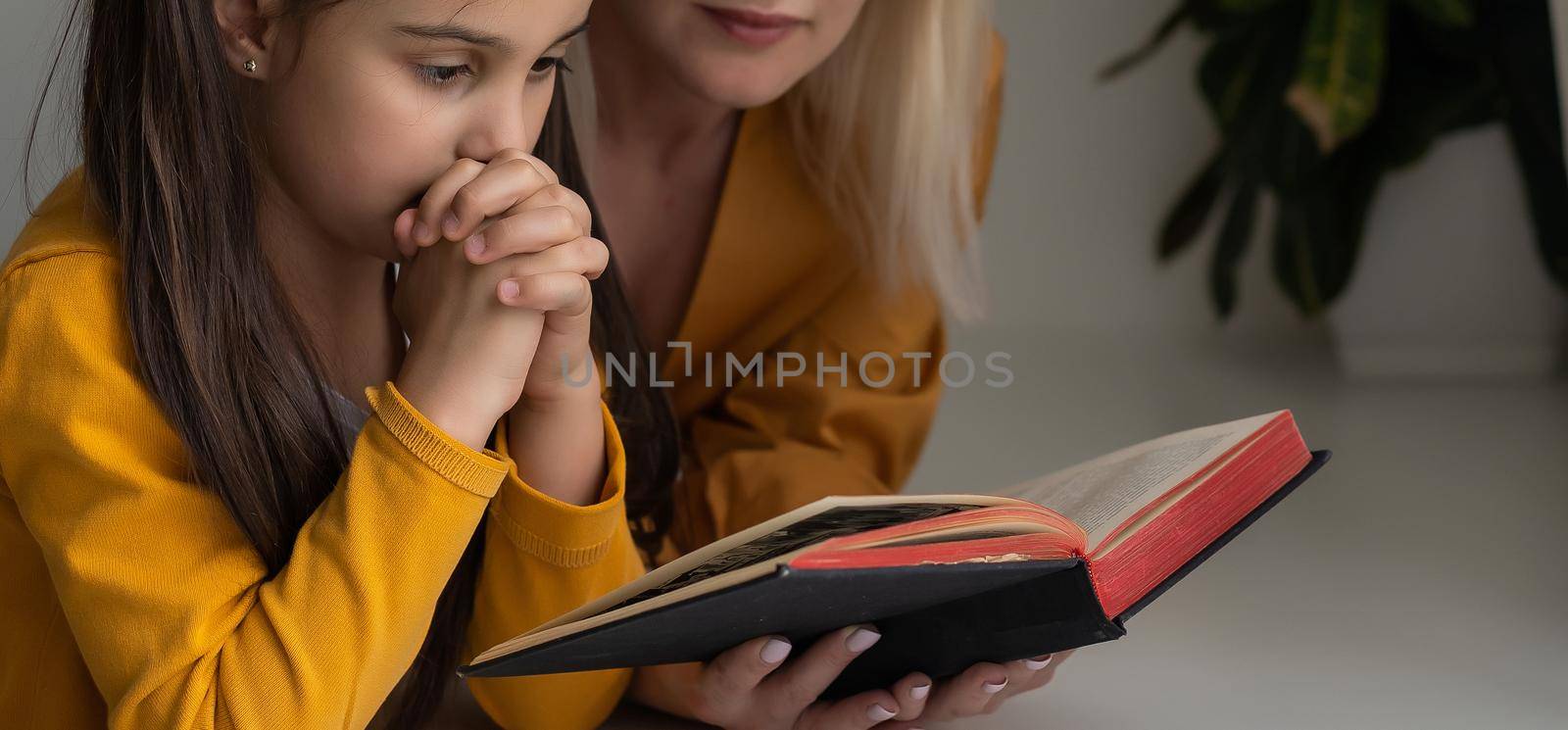 Religious Christian girl and her mother praying at home.