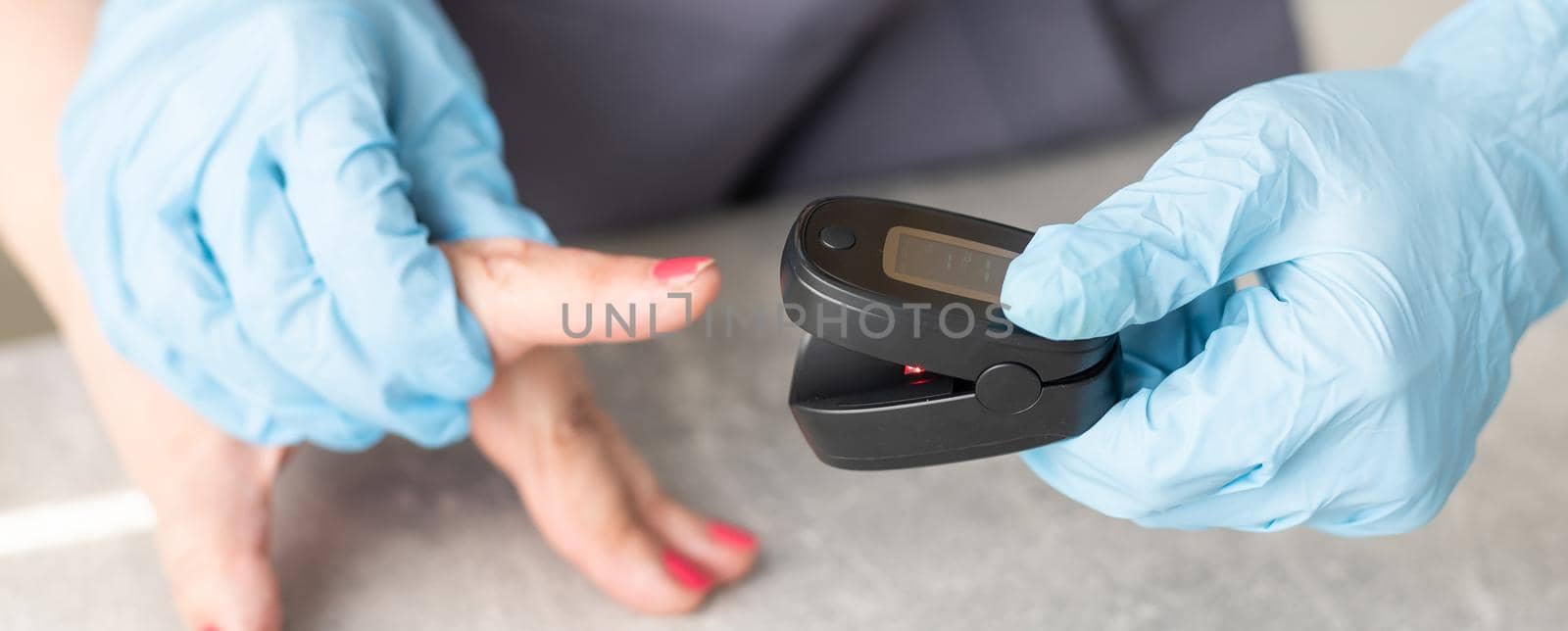 Medical help at home. Woman doctor in a medical mask measures the patient's pulse and oxygen saturation to middle aged woman using a pulse oximeter while sitting on sofa, healthcare concept.