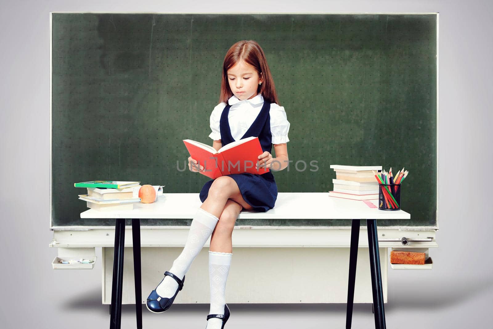 Young cute girl sitting at the table and reading a book by Taut