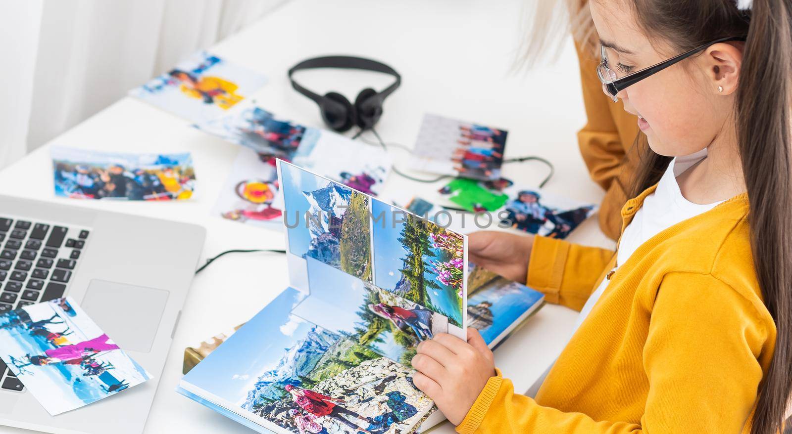 Young mother and her daughter looking photobook togerher at home. Family, childhood and leisure concept.