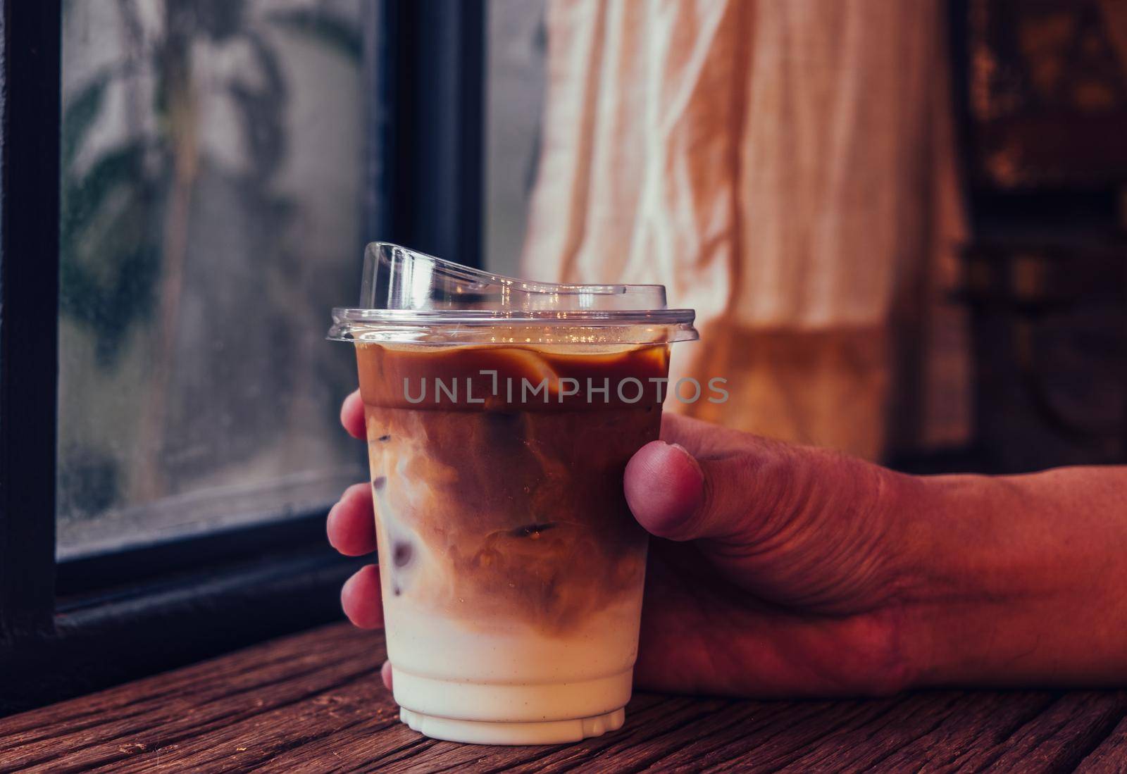 Hand hold iced latte coffee in a  tall glass. cold summer drink background