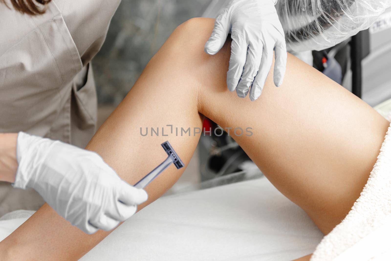 A girl at a laser hair removal procedure shaves her legs before the procedure. Hair removal with a razor. Master shaves client's legs by gulyaevstudio