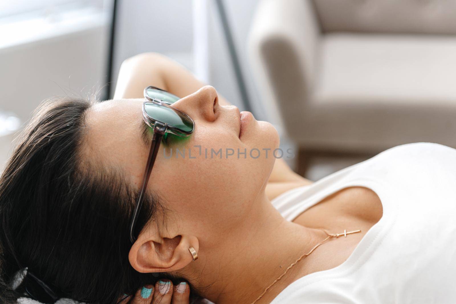 a girl in protective goggles for laser hair removal lies on her back during the procedure. A cosmetologist performs laser facial treatment for a woman at a beauty spa. Laser facial hair removal procedures. Facial rejuvenation medical correction. Close-up.