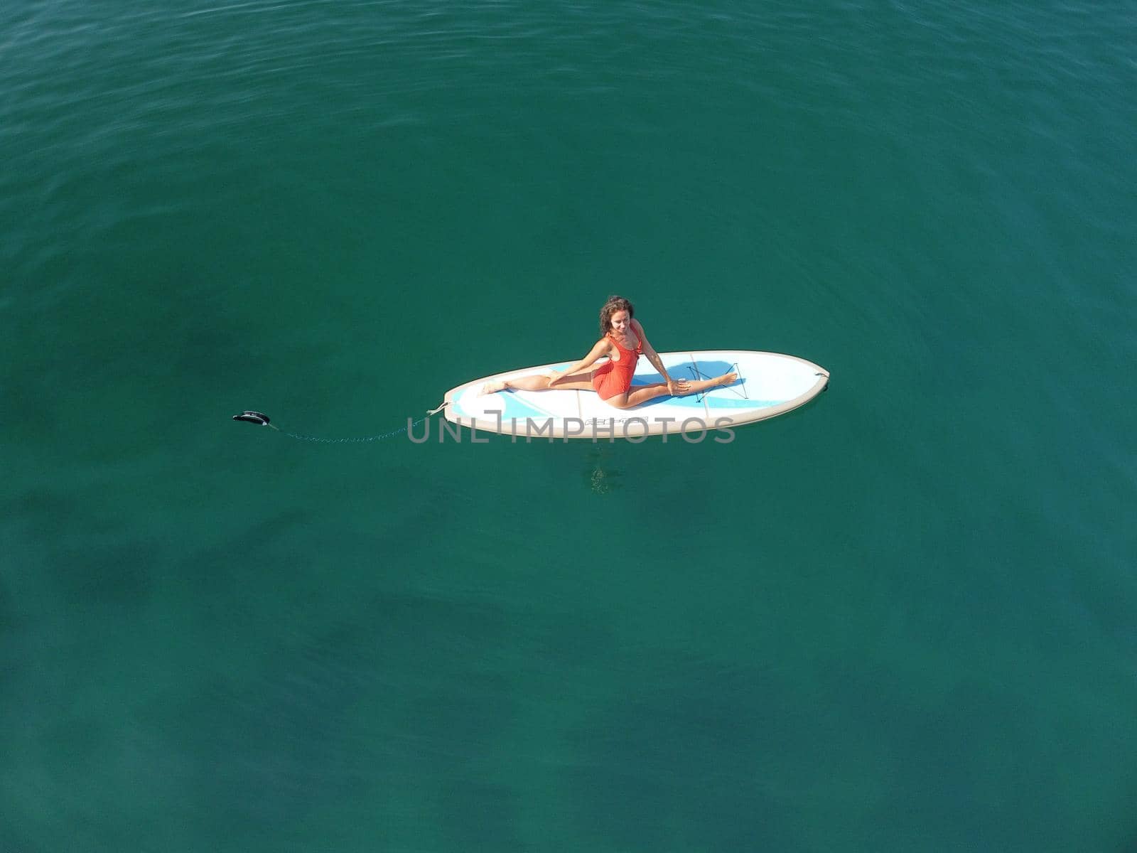 Aerial drone view on well looking middle aged woman with black hair in red swimsuit, swimming on sup in calm azure sea. Summer holiday vacation and travel concept. by panophotograph