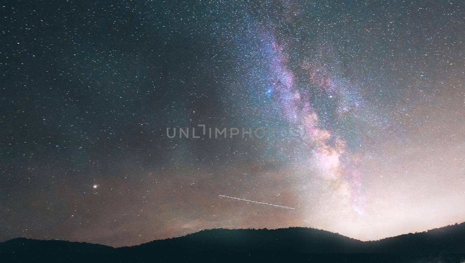 Night landscape with colorful Milky Way and yellow light at mountains. Starry sky with hills. Beautiful Universe.