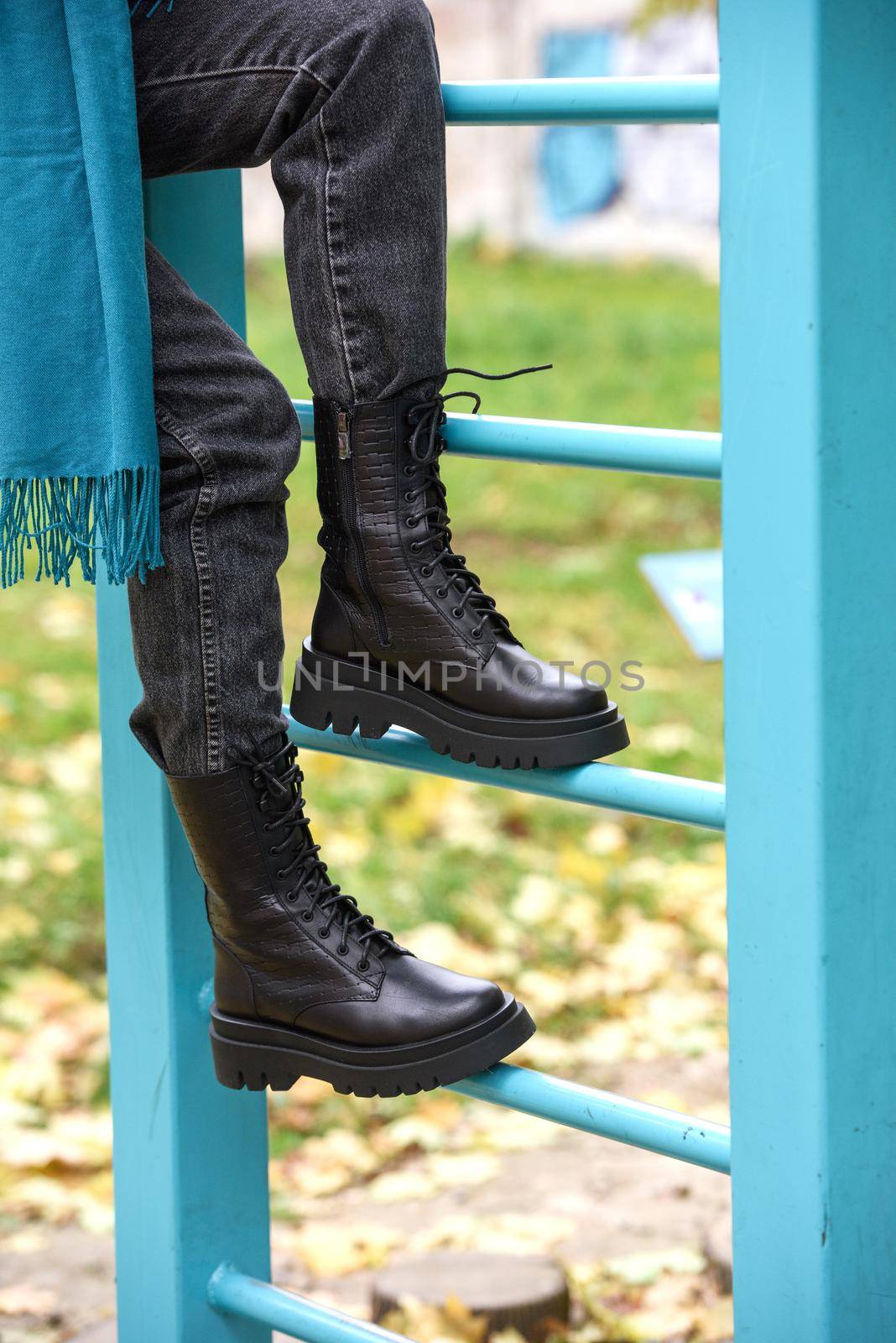 Slender female feets in military boots. street photo. woman wearing black jeans and blue scarf