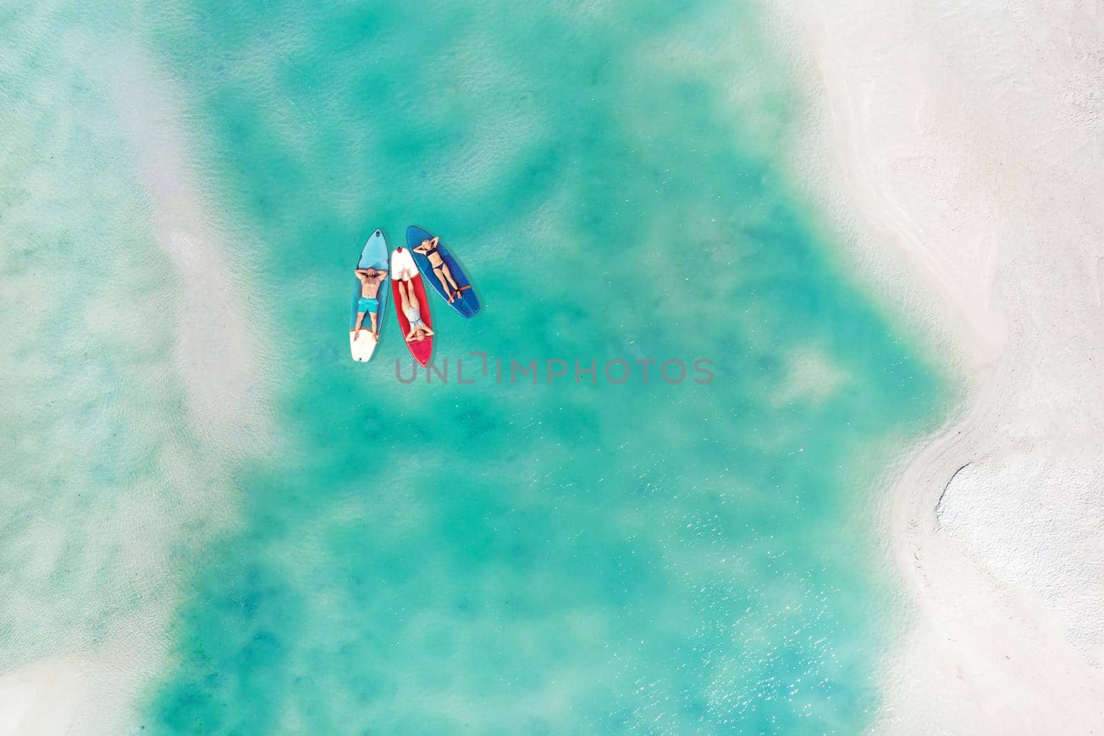 The family is resting lying on Sup boards in the turquoise sea. Three people ride sup boards in the ocean near the beach.