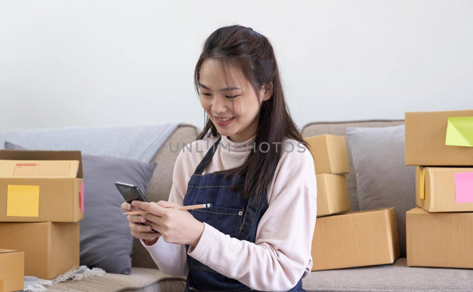 Happy young Asian woman entrepreneur, Smile for sales success after checking order from online shopping store in a smartphone at home office, Concept of merchant business online and eCommerce by wichayada