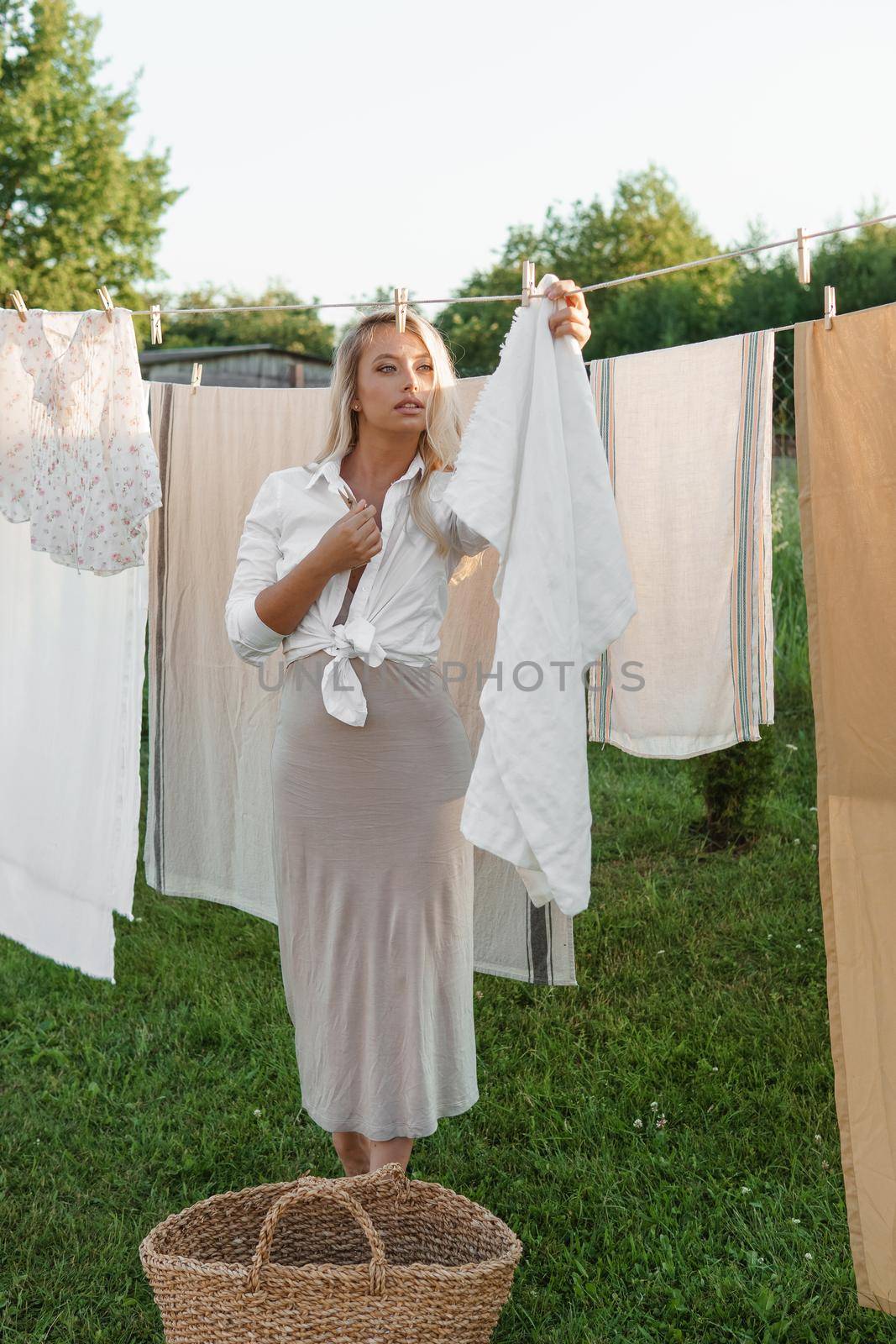 Laundry day. A woman hangs linen and towels on a tree in the courtyard of a village house. Summer cottage concept.