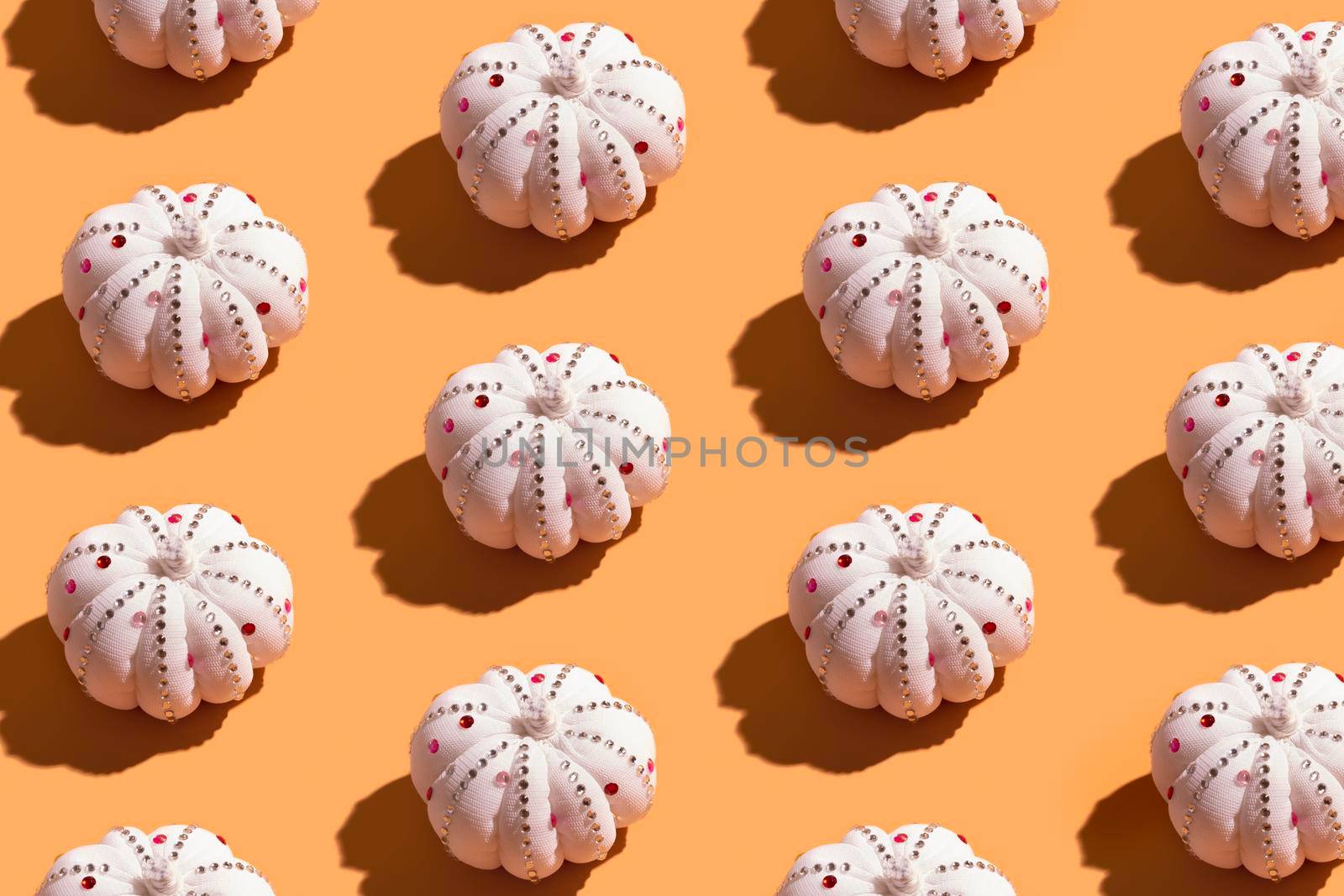 Pattern from white decorative textile pumpkin with shiny stones. Autumn minimal harvest concept. Orange background.